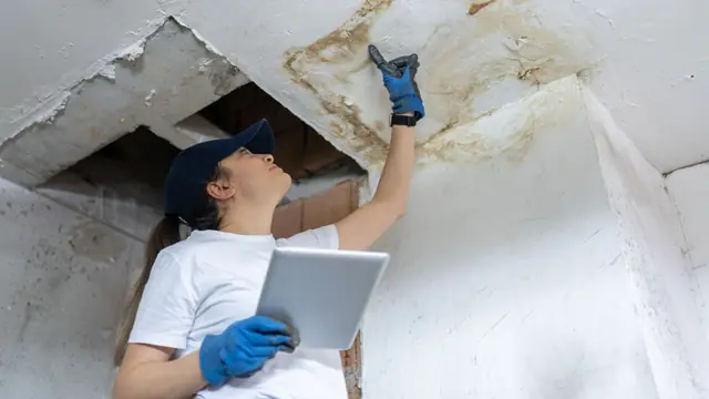 Inspector with a tablet checking a water damaged ceiling opening