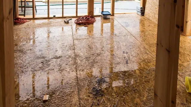Wet hardwood floor in a room with exposed wall framing